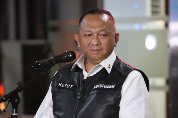 Ein Mann in einem schwarzen Westen und weißem Hemd steht vor einem Mikrofon und sieht besorgt aus, mit einem unscharfen Hintergrund.