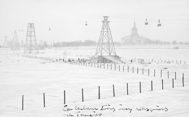 Schwarze und weiße Fotografie eines Ski lifts in einem verschneiten Feld mit Stützpfählen, Überseilbahn, Bäumen und einem Gebäude im Hintergrund, mit Text am unteren Rand.
