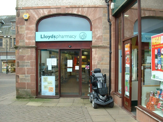 Ein Apothekenladen mit einem Fahrzeug davor und einem Gebäude in der linken Ecke.