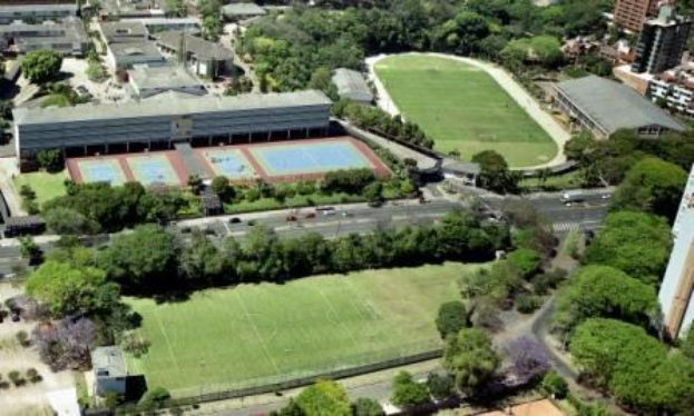 Luftaufnahme eines Fußballfeldes an der Universität Sydney, umgeben von Bäumen, Gebäuden und Fahrzeugen, mit einem neuen Sportkomplex unter construction.