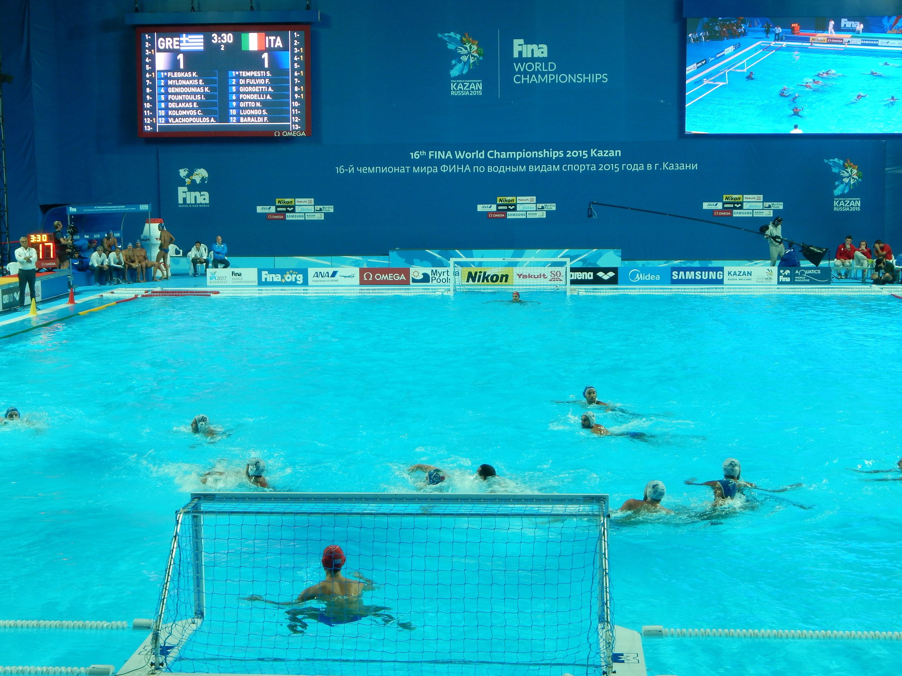 Wasserballspieler bei der 2016 FINA Weltmeisterschaft in Kazan im Pool gegeneinander antretend, mit Zuschauern und einer Anzeigetafel im Hintergrund.