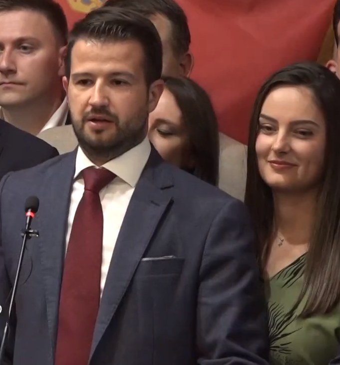 Ein Mann im Anzug spricht an einem Podium mit einem Mikrofon zu einer Menge hinter einem Banner, wahrscheinlich über ein Regierungsoziales-Medium-Verbot.