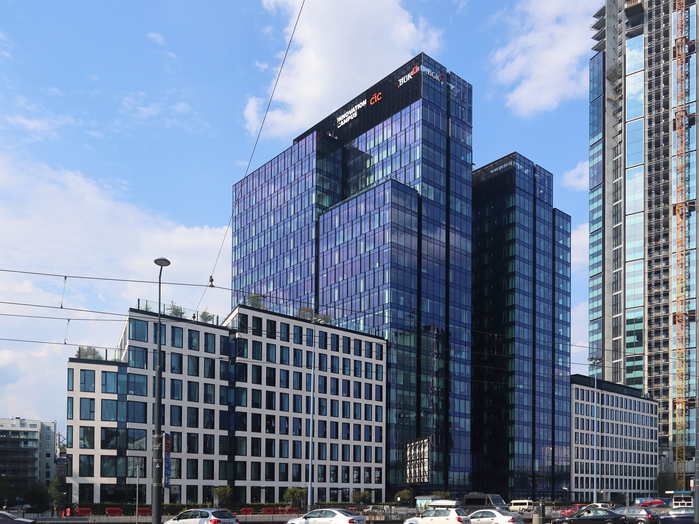 Hauptsitz der Deutschen Bank in Frankfurt, Deutschland, ein großes Gebäude mit vielen Fenstern, umgeben von Straßeninfrastruktur, Fahrzeugen, Grünflächen und einem bewölkten Himmel.
