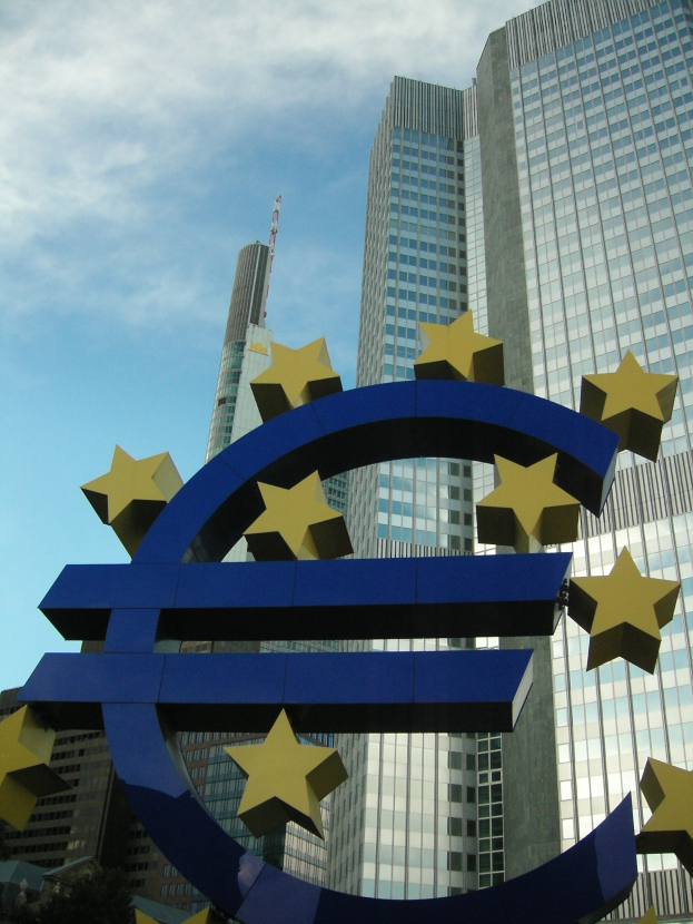 Eurozeichen vor dem Hauptquartier der Europäischen Zentralbank in Frankfurt, Deutschland, mit Bäumen und bewölktem Himmel im Hintergrund.