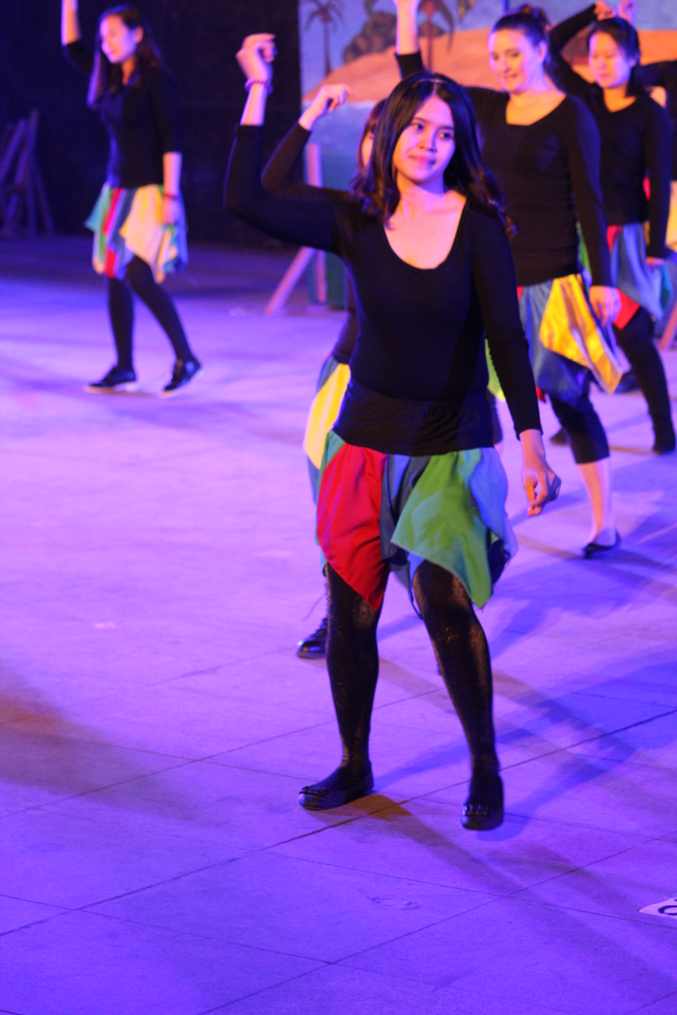 Eine Gruppe junger Frauen tanzt auf einer Bühne, trägt Schuhe und hat ein Gemälde im Hintergrund.