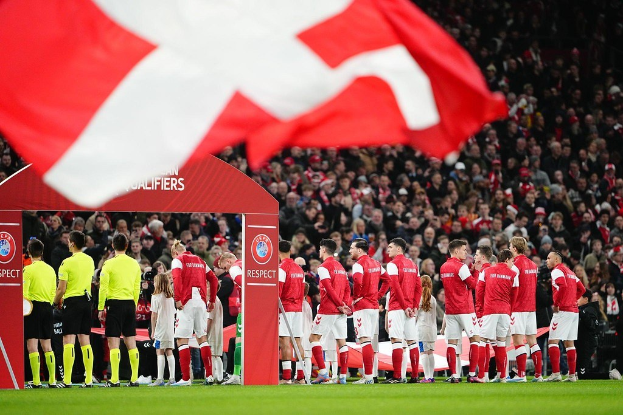 Eine Gruppe von Menschen auf einem Fussballfeld mit einer roten und weißen Flagge im Vordergrund, einem Bogen mit der Aufschrift "Bayern München vs Bayern München Wetten & Vorschau" im Hintergrund und einer großen Stadionmenge.
