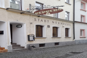 Außenansicht eines Gebäudes mit einem "Stadt Nurnberg"-Schild, Fenstern, einer Tür, einer Treppe und einem Müllcontainer im Vordergrund.