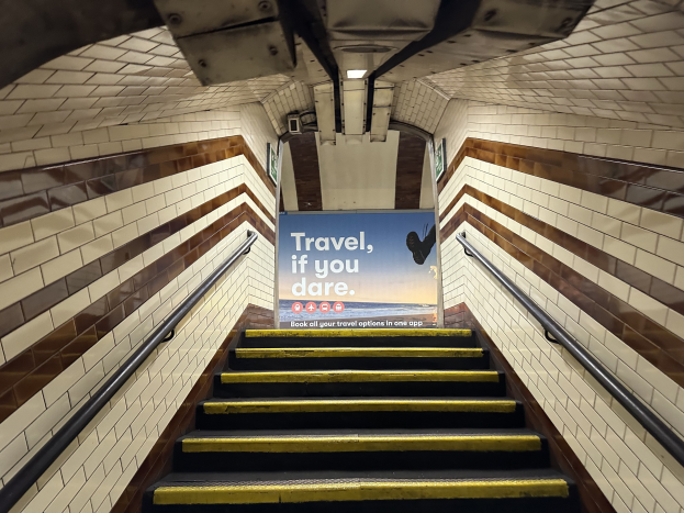 Eine Treppe in einer U-Bahn-Station mit einem 'Reise, wenn du wagst' Schild oben, flankiert von Geländern und U-Bahn-Stationswänden im Hintergrund.