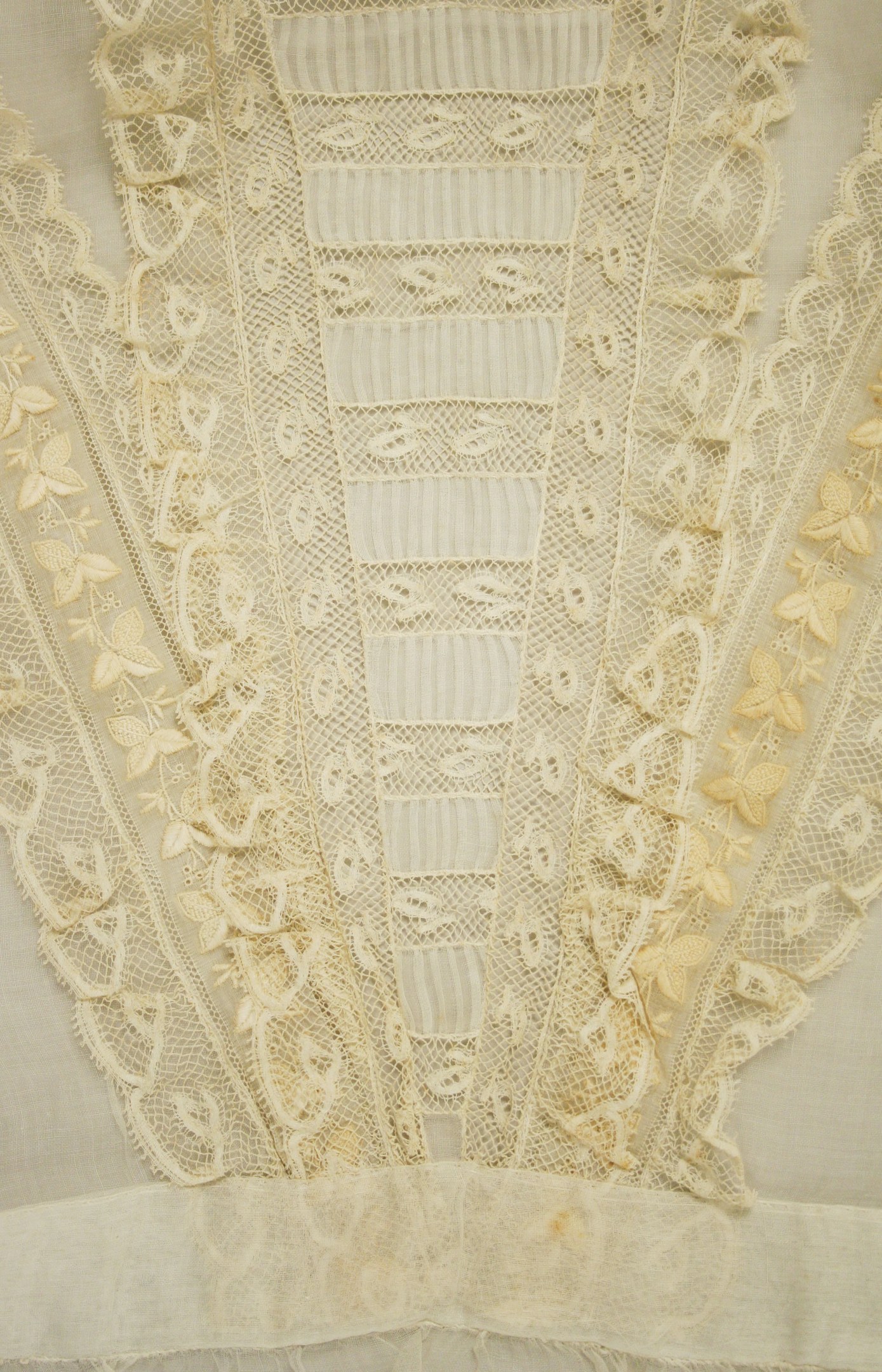 Nahaufnahme eines weißen Kleides mit zarter, detailreicher Spitzenverzierung mit verschiedenen Formen und Mustern auf leichtem, luftigem Stoff.