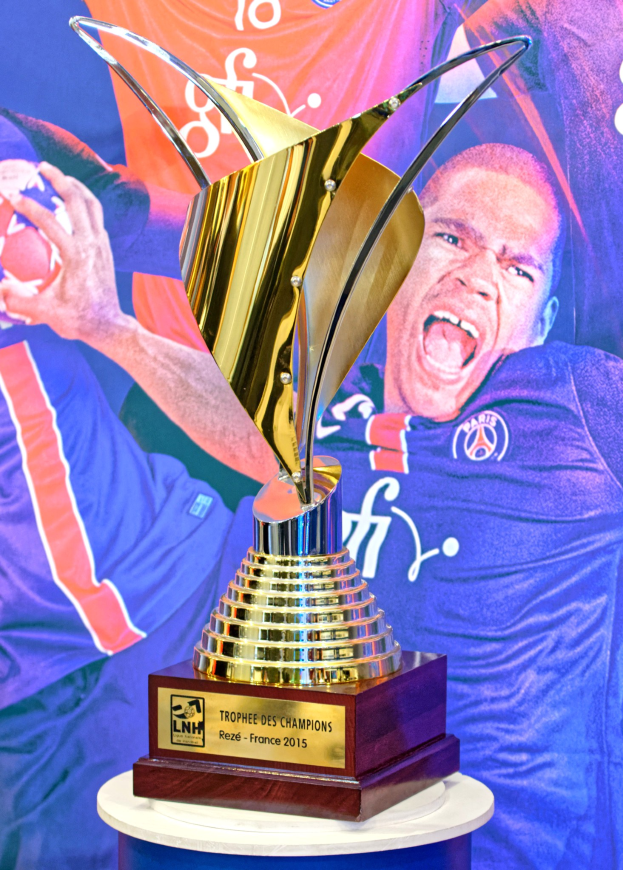 Eine silberne Trophäe auf einem Tisch mit einem unscharfen Banner im Hintergrund, das ein Personenbild zeigt.