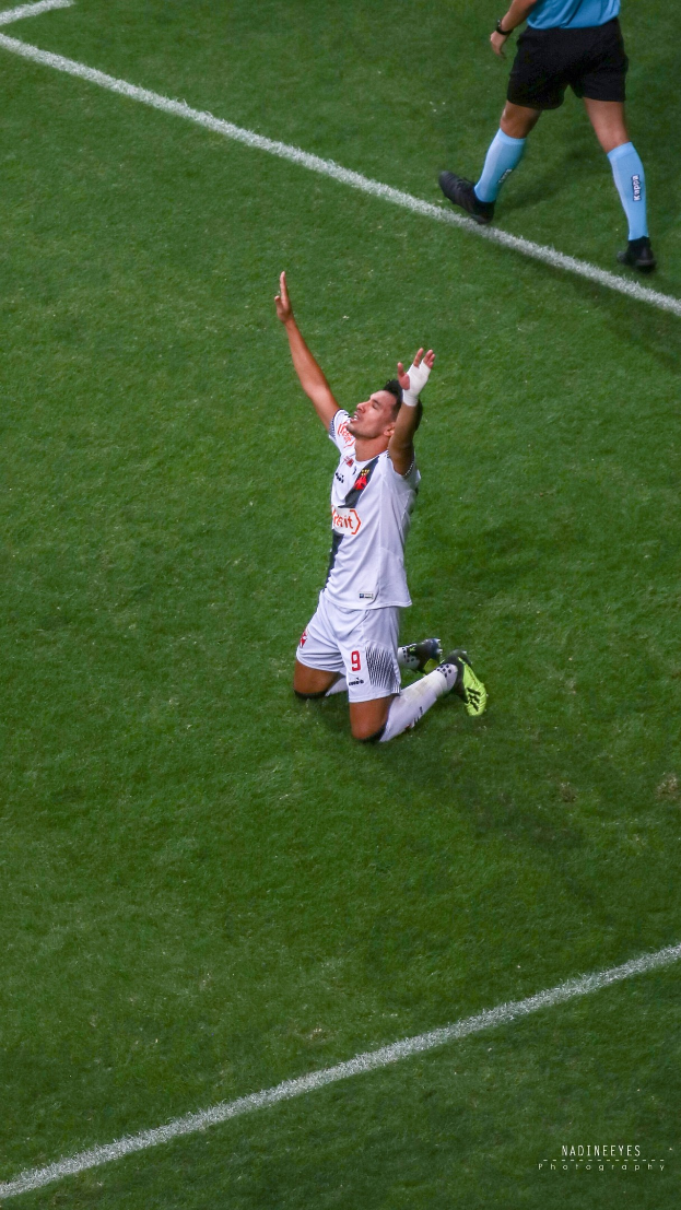 Ein Fußballspieler kniet auf dem Boden und streckt die Arme aus, um zu feiern, trägt eine Sportuniform und Schuhe.
