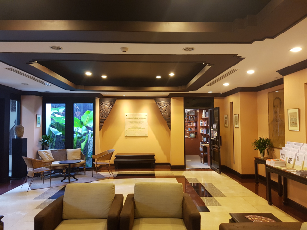 Eine Hotellobby mit Sitzbereichen, Dekorationspflanzen, Bücherregalen, Wandkunst und Seitentisch-Dekoration, beleuchtet von Deckenlampen und natürlichem Sonnenlicht durch Fenster und Türen.