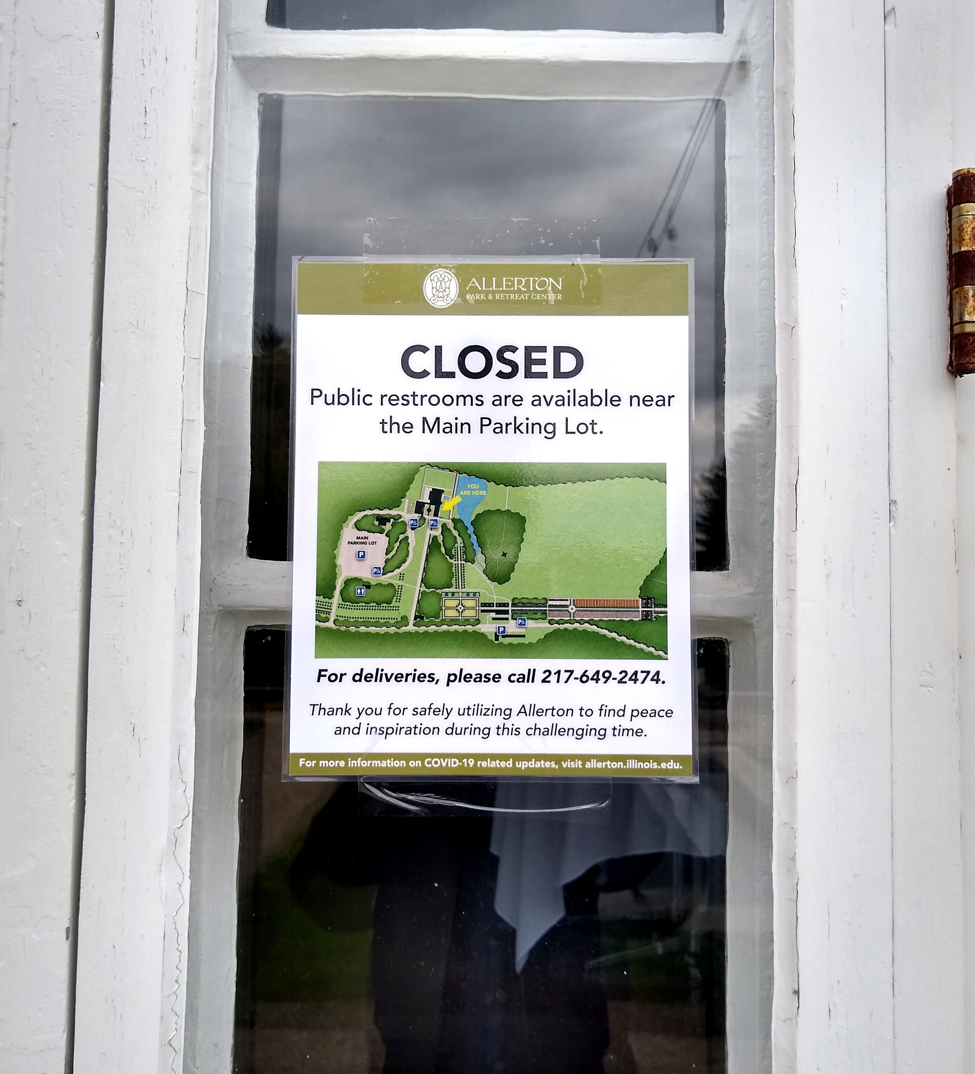 Glasstür mit einem Schild "Geschlossene öffentliche Toiletten in der Nähe des Hauptparkplatzs" und einem unklaren Objekt auf der rechten Seite.