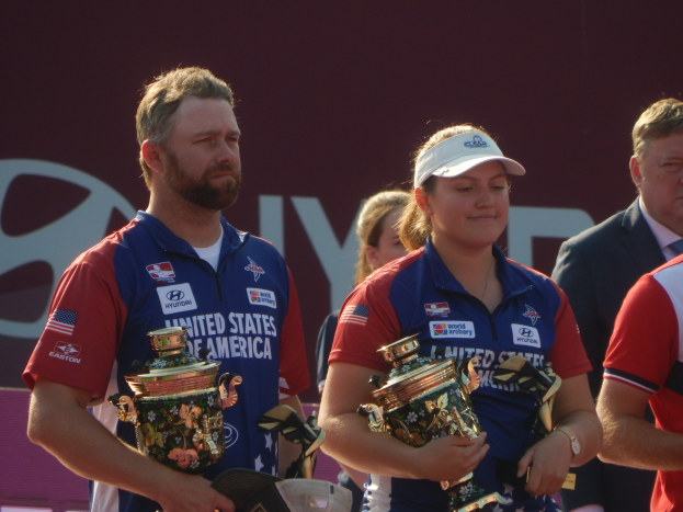 Eine Gruppe von Menschen, die Pokale halten, vor einem Hintergrund mit der Aufschrift "Weltmeisterschaften im Bogenschießen"