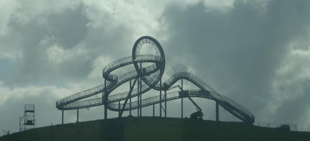 Eine Achterbahn auf dem Höhepunkt eines Hügels unter einem bewölkten Himmel, umgeben von Stützstrukturen.
