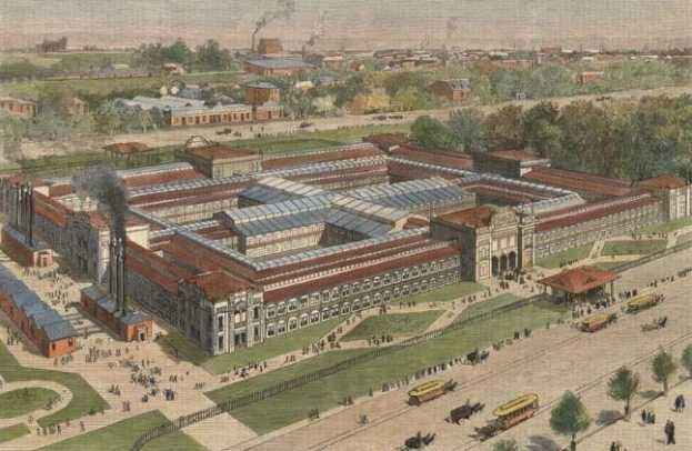 Luftaufnahme eines großen Gebäudes in einem Park, umgeben von Bäumen, Gras und Fahrzeugen, mit Menschen, die herumlaufen und dem Himmel im Hintergrund; das Gebäude ist wahrscheinlich ein Gefängnis, wie durch Text am unteren Rand angezeigt.