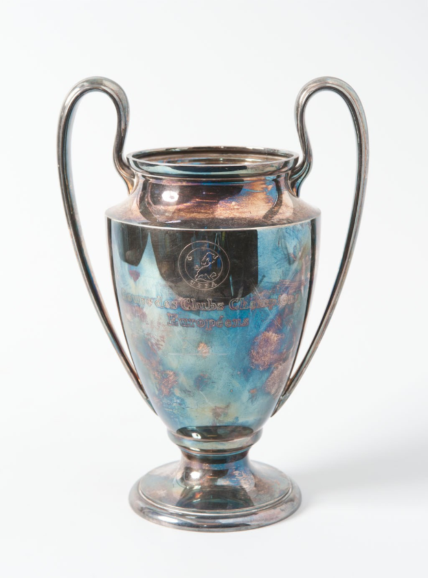 UEFA Champions League-Trophäe, ein stählerner Pokal mit zwei Griffen, blau-silbernes Farbschema, mit "UEFA Champions League" beschriftet, auf einem weißen Hintergrund.