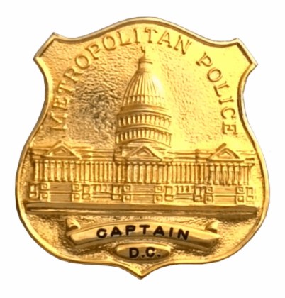 Goldenes Polizeidienstabzeichen mit 'Metropolitan Police Captain' eingraviert, mittig auf weißem Hintergrund.