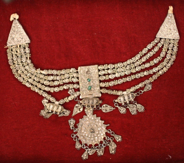 Silberne Halskette mit Smaragden und Diamanten auf einem roten Samt-Hintergrund.