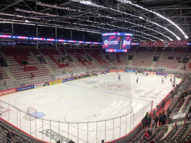 Eishockeyspiel in einer großen Arena zwischen den St. Louis Blues und den Detroit Red Wings, mit Zuschauern auf den Sitzen und Stehplätzen in der Nähe der Eisfläche, umgeben von einem Zaun und einem Anzeigebildschirm.