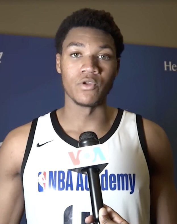 Ein Mann in einem wei\uml;en Tanktop h"alt ein Mikrofon und spricht mit der Medien bei der NBA All-Star Game 2019, mit einem Banner und einer Wand im Hintergrund.