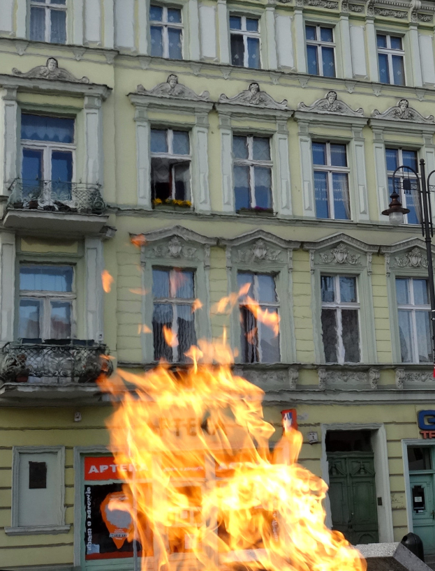 Ein großes Feuer brennt vor einem Gebäude mit Fenstern, Türen, einem Laternenpfahl und einer Tafel.
