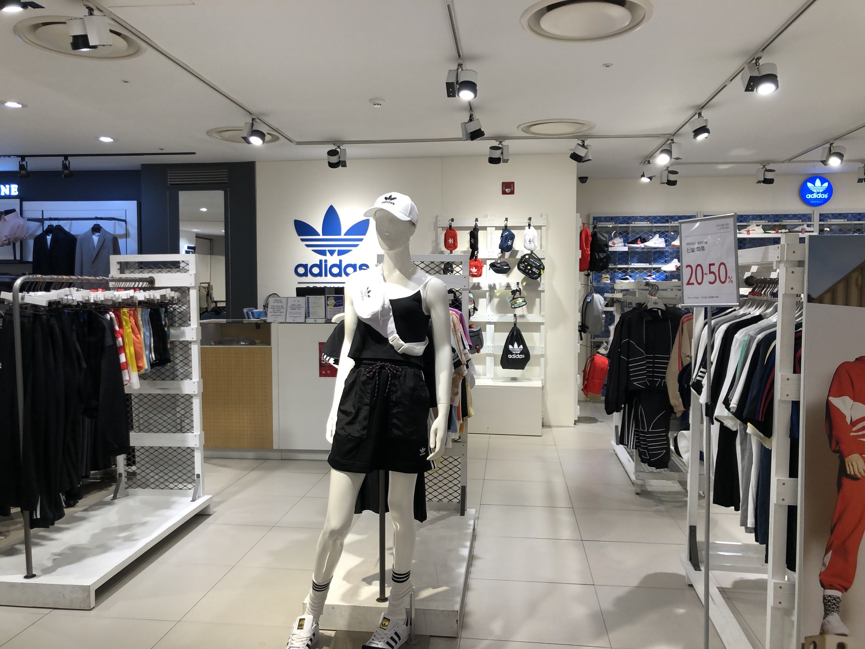 Innenansicht eines adidas-Ladens in Singapur mit Schaufensterpuppen, Kleiderständern, einem Textbrett auf der rechten Seite und Deckenbeleuchtung.