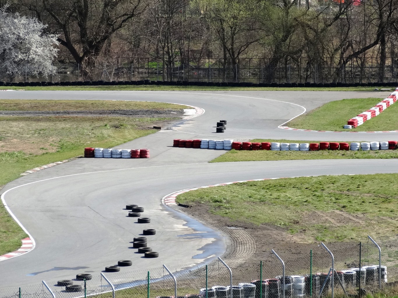 Rennbahn mit zahlreichen Reifen auf der Oberfläche, umgeben von Gras und Maschendrahtzaun und mit Bäumen im scenischen Hintergrund.