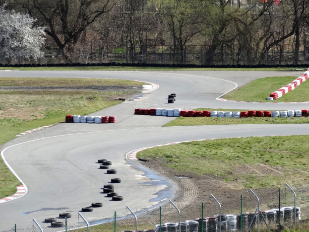 Rennbahn mit zahlreichen Reifen auf der Oberfläche, umgeben von Gras und Maschendrahtzaun und mit Bäumen im scenischen Hintergrund.