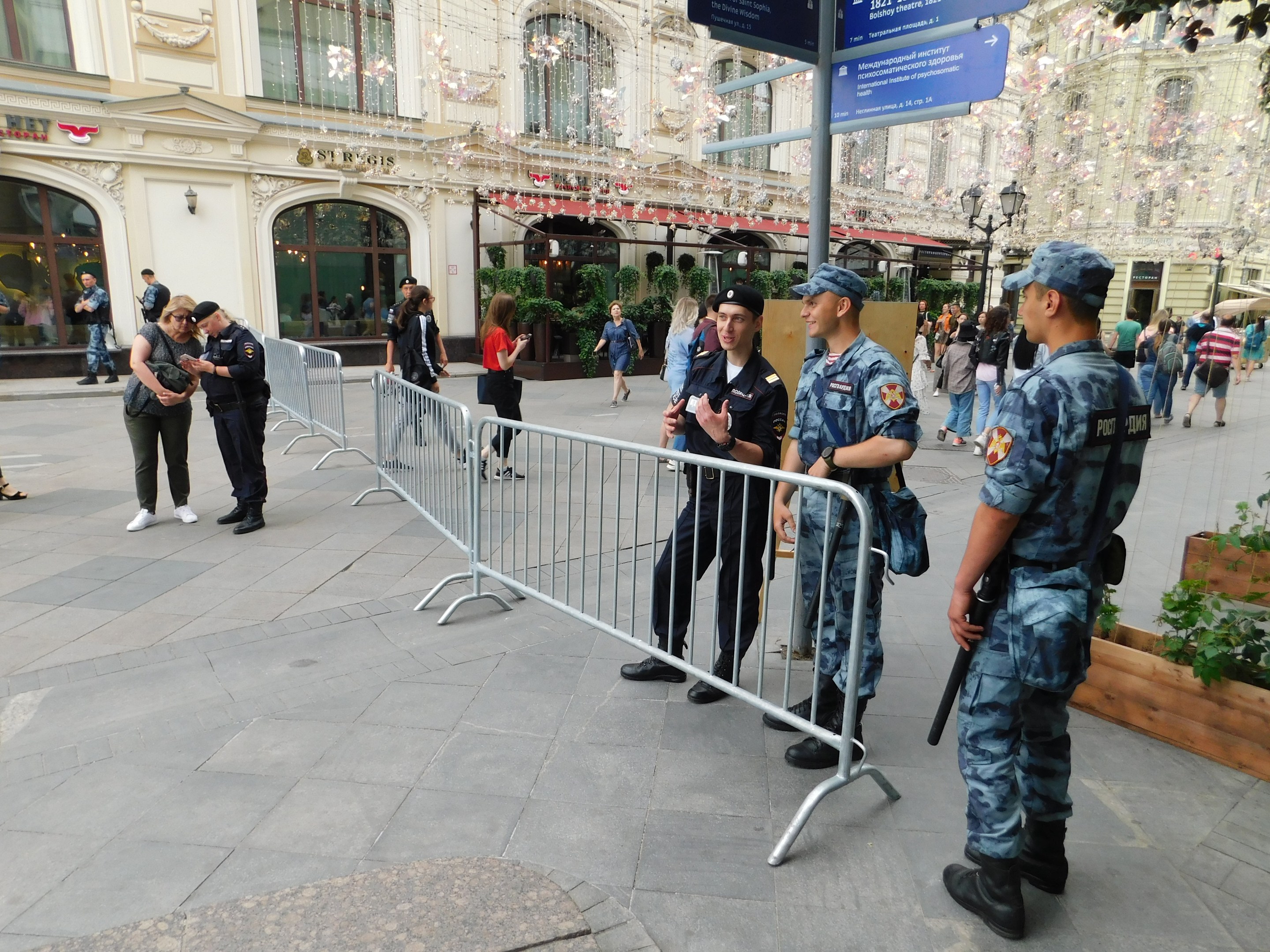 Polizisten vor einer Menschenmenge, einige mit Waffen, mit Absperrungen und Schildern im Vordergrund und Gebäuden, Laternen, Pflanzen und Bäumen im Hintergrund während eines Anti-Terror-Einsatzes in Wien, Österreich.