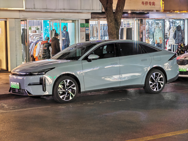 Ein Mitsubishi Lancer EV Elektroauto auf einer Straße bei Nacht geparkt, umgeben von Gebäuden, Geschäften, Schaufensterpuppen mit Kleidern, Schildern, Lichtern und anderen Gegenständen.