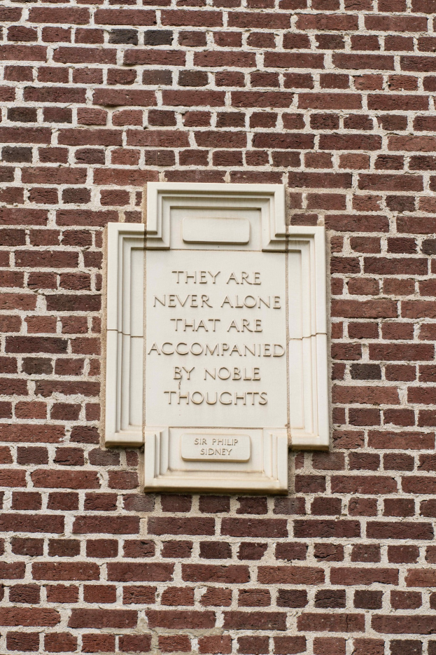 Steintafel an einer Backsteinwand mit der eingravierten Inschrift "Sie sind nie allein, die von edlen Gedanken begleitet sind".