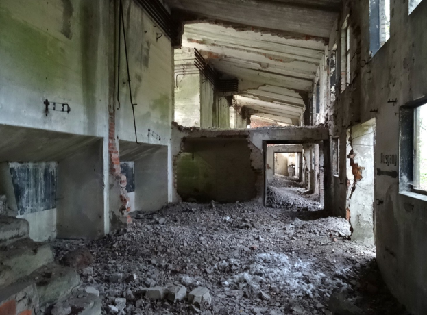 Altes Gebäude mit umfangreichen Trümmern, zerbrochenen Fenstern und verstreutem Schutt, was auf schweren Verfall hinweist.