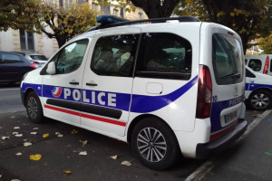 Polizeifahrzeug auf einer Stadtstraße mit Gebäuden, Bäumen und welken Blättern geparkt.