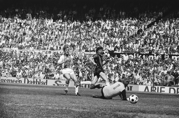 Schwarzes und weißes Foto von Männern, die auf einem Feld Füßball spielen, mit Zuschauern im Hintergrund und einem Banner mit der Aufschrift "Bundesliga 1978-79 Ajax 1-1 Hannover 96."
