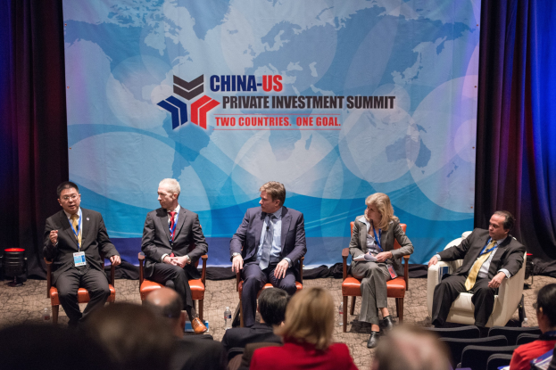 Gruppe von Menschen, die auf Stühlen sitzen und auf einen Bildschirm mit Text und einer Karte schauen, mit Vorhängen im Hintergrund, was auf einen China-US-Privatinvestment-Gipfel hinweist.