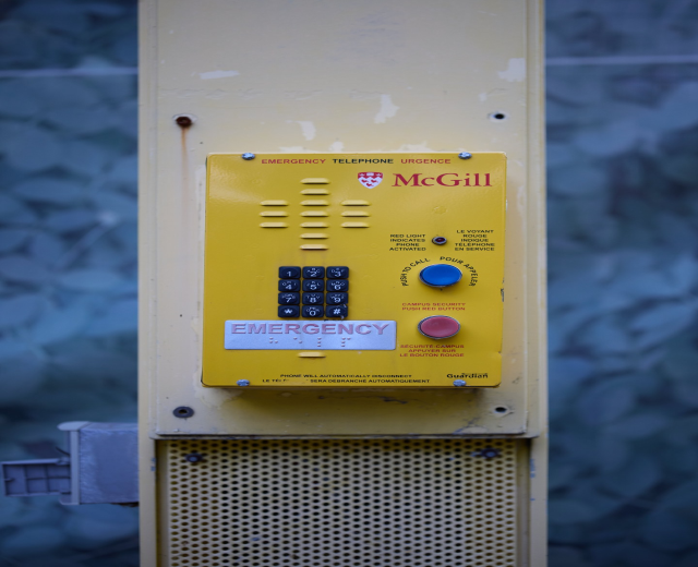 Gelber Notrufhörer an einer Gebäudewand montiert, mit strukturiertem Hintergrund.