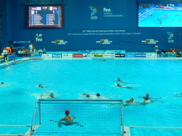 Gruppe von Menschen, die Wasserball in einem Pool während der 2016 FINA-Weltmeisterschaften in Kazan spielen, mit einem Netz, das den Pool teilt, und Zuschauern, die auf der linken Seite sitzen.