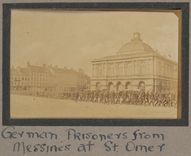 Deutsche Kriegsgefangene aus Messines vor einem Gebäude mit einem klaren blauen Himmel im Hintergrund.
