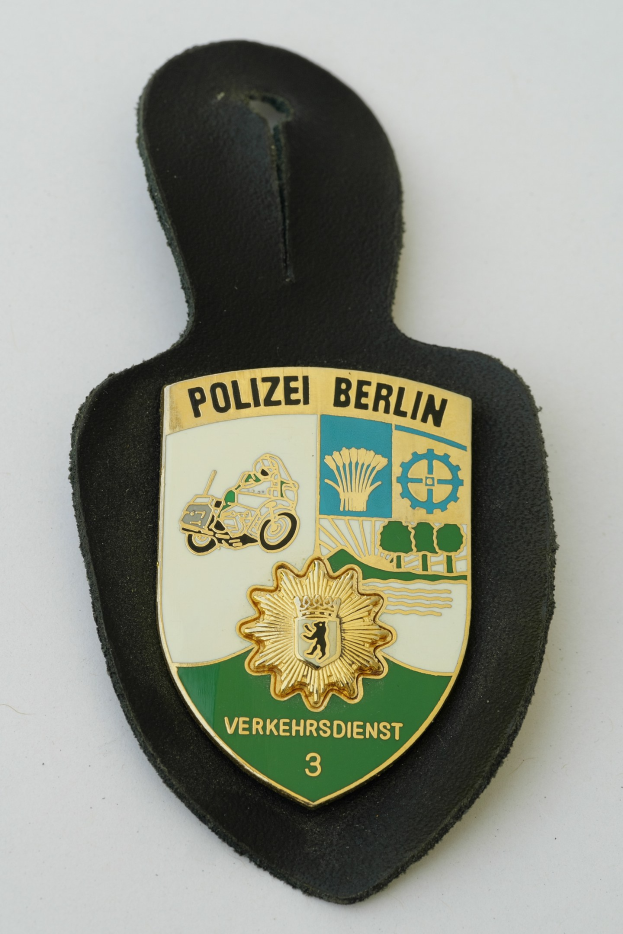 Polizei Berlin Abzeichen mit einem blauen Schild, weißer Umrandung, zentralem weißen Stern und schwarzer fetter Schrift auf einer Oberfläche.