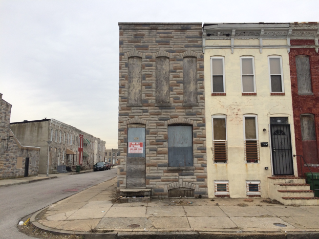 Ein altes, baufälliges Gebäude an einer Straßenecke mit zerbrochenen Fenstern, bröckelnden Wänden, vorbeifahrenden Fahrzeugen, Mülltonnen an der Straße und einem klaren blauen Himmel im Hintergrund.