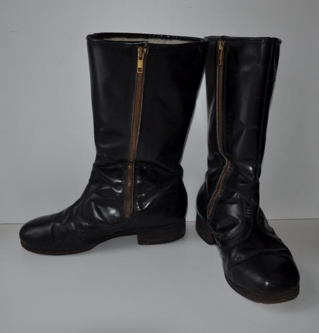 Schwarze Lederstiefel mit silbernen Reißverschlüssen auf einer weißen Oberfläche, mit einem glänzenden Finish und einem schlanken Design.