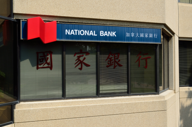 Ein modernes Gebäude mit Glasfenstern, die ein 'National Bank'-Schild in Englisch und Chinesisch zeigen, mit einer Pflanze links, die eine neue Filiale in Hong Kong ankündigt.