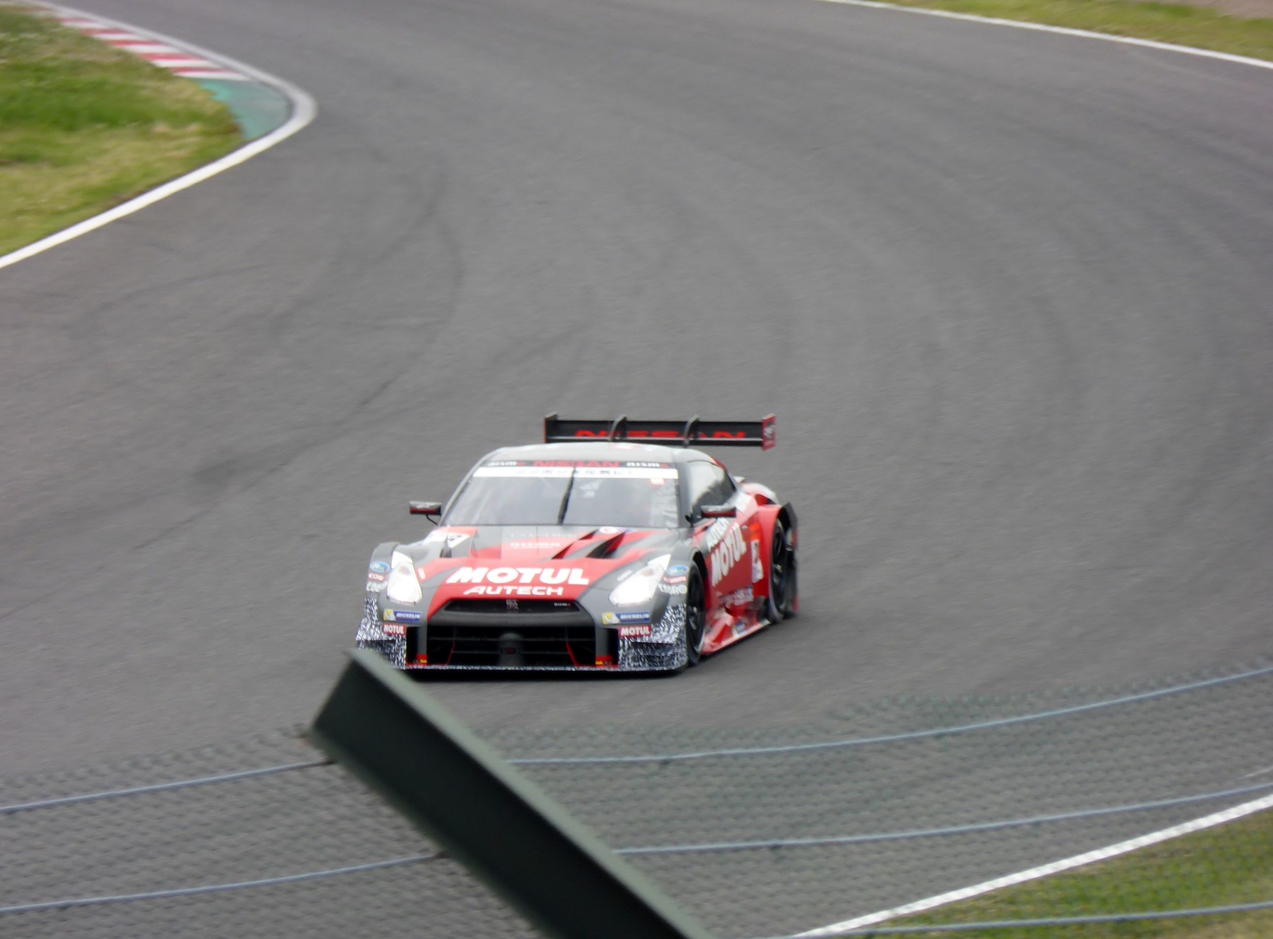 Ein Nissan GT-R Nismo GT3 Rennauto auf der Nürburgring 24 Stunden Strecke, umgeben von grünem Gras auf beiden Seiten.