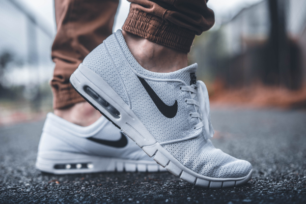 Eine Person trägt Nike SB Stefan Janoski Max-Schuhe in Wolf Grau/Schwarz-Weiß vor einem unscharfen, träumerischen Hintergrund.